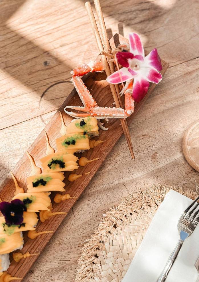 Un plateau de sushis vu de haut sur une table en bois avec une fleur tropicale.