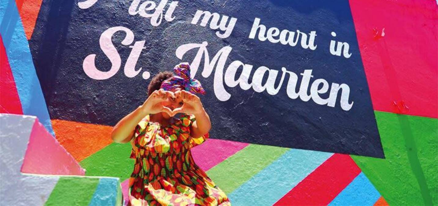 Une femme forme un coeur avec ses mains devant une fresque colorée à Saint-Martin