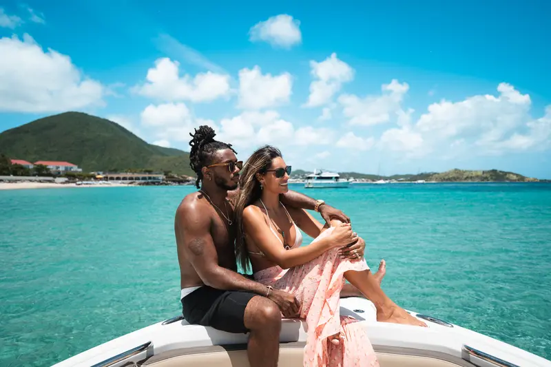 Couple sitting at the bow of the Aura private boat, turquoise sea behind them.