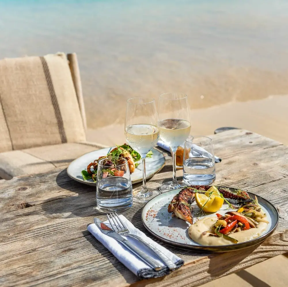 Grilled fish and white wine on a wooden table by the beach.