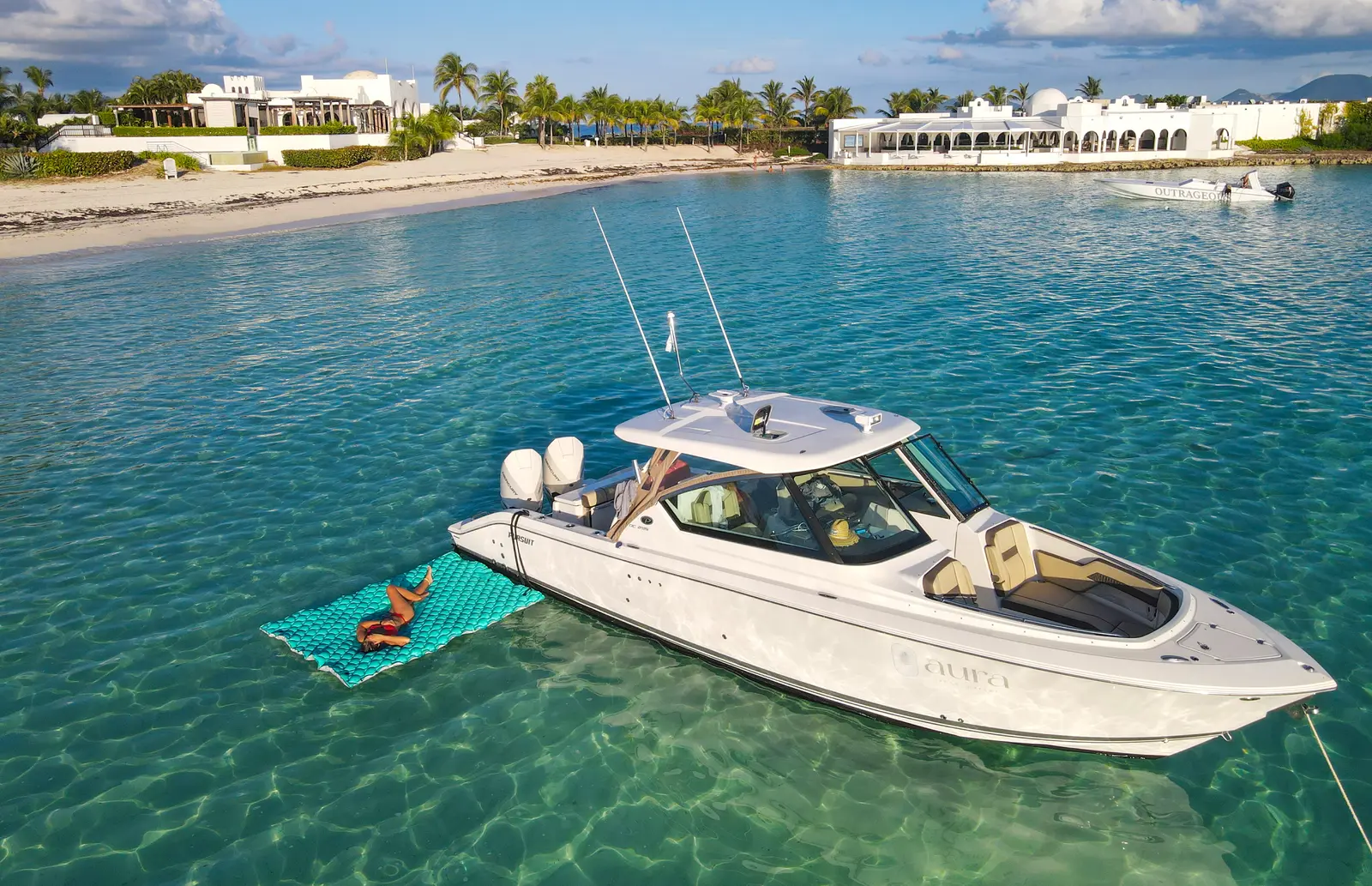 The Aura boat anchored in clear water near a beach.
