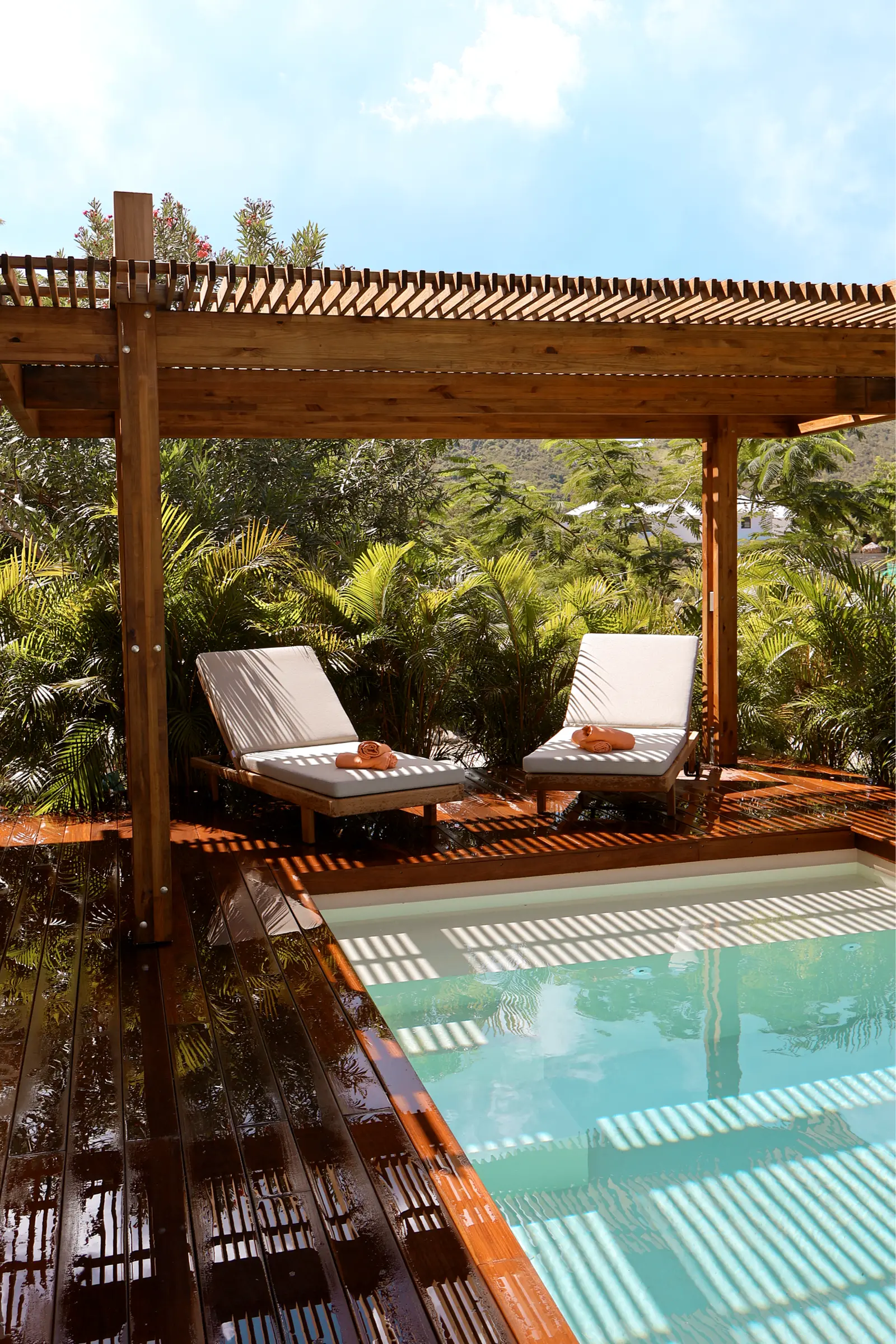 Two loungers on a wooden terrace by the pool.